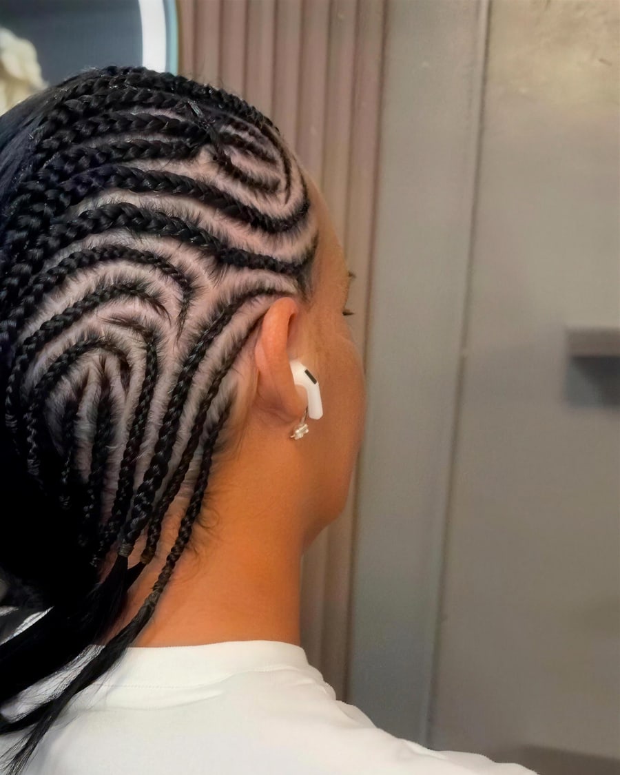 Curved feed-in cornrows braided into a swirling pattern, side view with clean parting